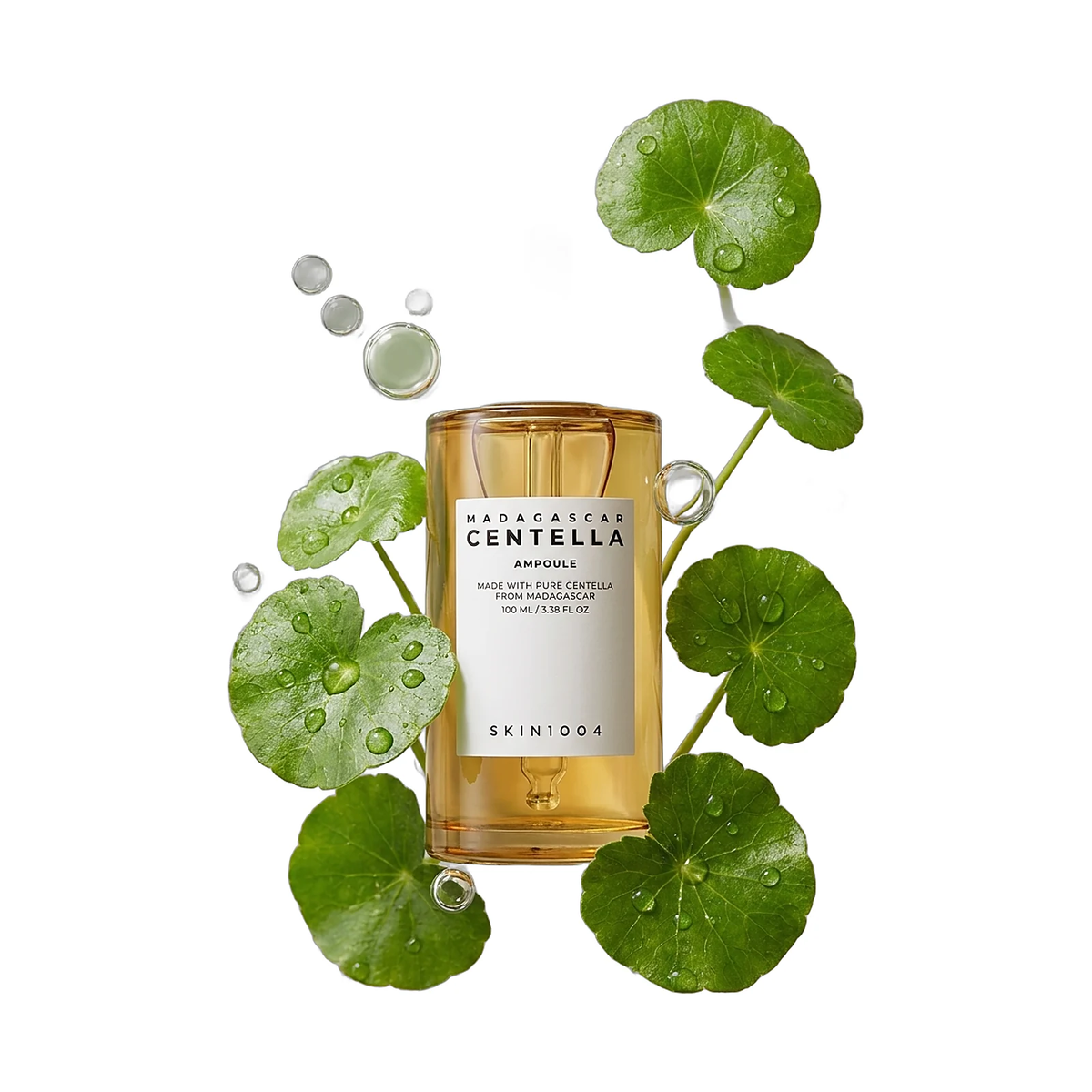 Ampoule SKIN1004 Madagascar Centella mise en scène, entourée de feuilles de centella et de gouttelettes